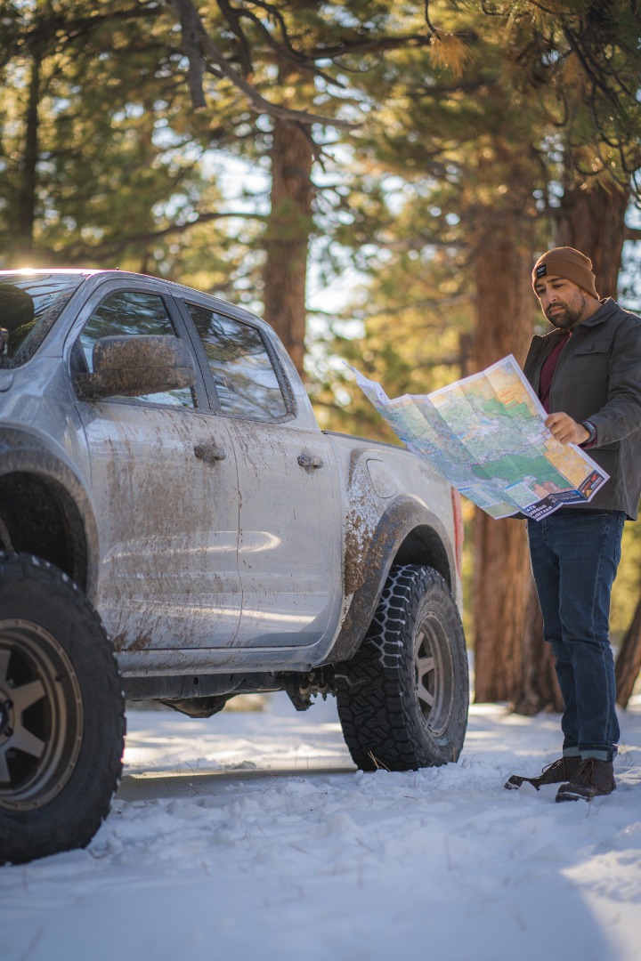 A man reading paper map off-road in the snow next to a truck