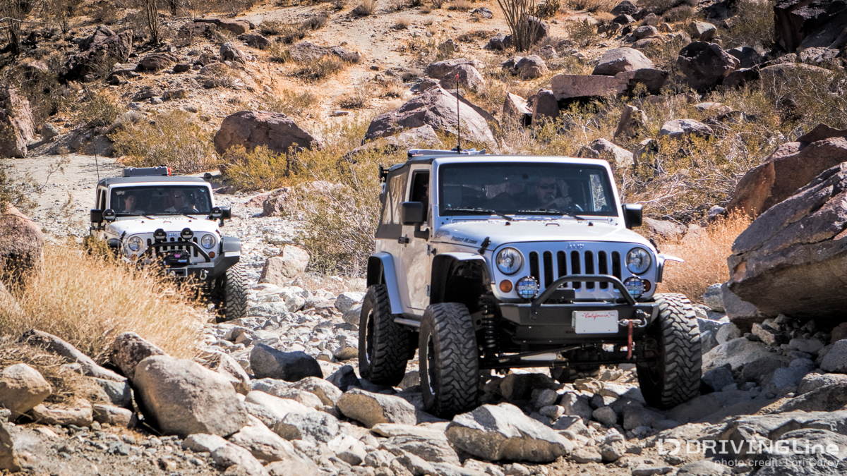 Two Jeep Wranglers driving over rocks on a trail